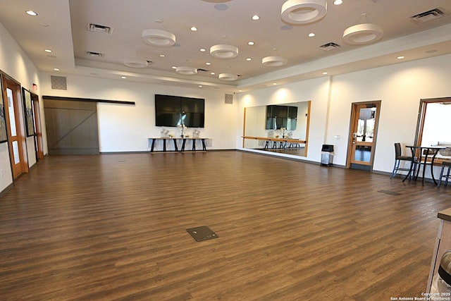 exercise area with dark hardwood / wood-style floors, a barn door, and a raised ceiling