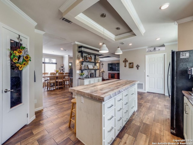 kitchen with pendant lighting, black refrigerator, a center island, white cabinets, and a kitchen bar