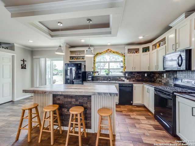 kitchen featuring a raised ceiling, a center island, a breakfast bar area, and black appliances