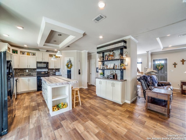 kitchen with pendant lighting, a center island, a tray ceiling, black appliances, and white cabinets