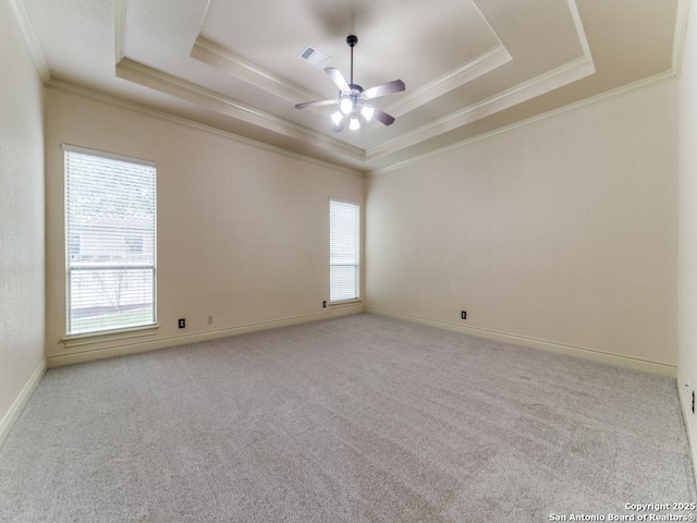 empty room with a tray ceiling, ornamental molding, light colored carpet, and ceiling fan