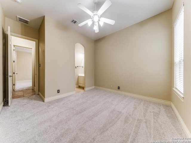 unfurnished bedroom featuring ensuite bath, light colored carpet, and ceiling fan