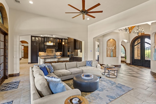 living room featuring a towering ceiling, ceiling fan with notable chandelier, and french doors