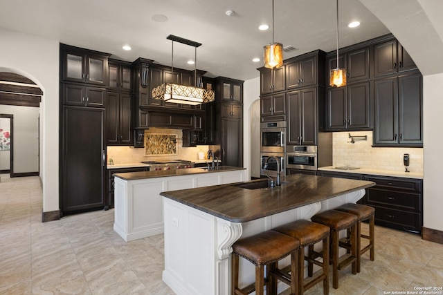 kitchen with pendant lighting, stainless steel appliances, sink, and a center island with sink