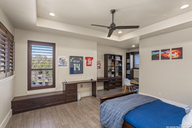 bedroom with a tray ceiling, light hardwood / wood-style floors, and multiple windows