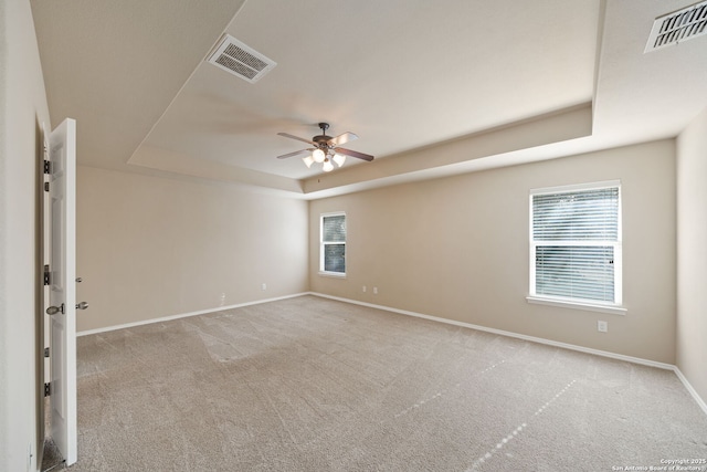 empty room featuring light carpet, a raised ceiling, and ceiling fan