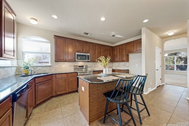 kitchen featuring a kitchen island, sink, dark stone countertops, light tile patterned floors, and stainless steel appliances