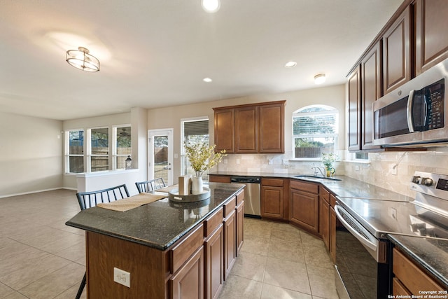 kitchen with light tile patterned floors, appliances with stainless steel finishes, a kitchen breakfast bar, tasteful backsplash, and a kitchen island