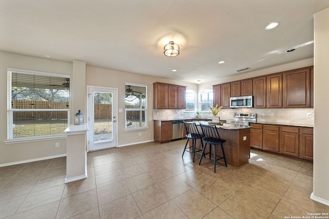 kitchen featuring appliances with stainless steel finishes, a center island, tasteful backsplash, a kitchen bar, and light tile patterned flooring