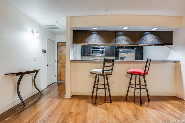 kitchen featuring stainless steel appliances, a breakfast bar, kitchen peninsula, and light hardwood / wood-style flooring