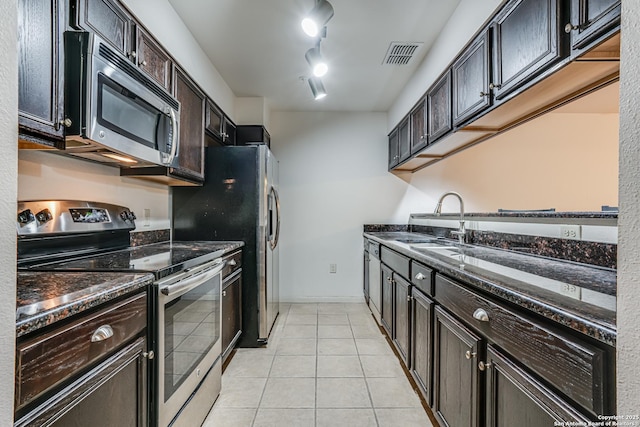 kitchen featuring appliances with stainless steel finishes, sink, dark stone countertops, light tile patterned floors, and dark brown cabinets