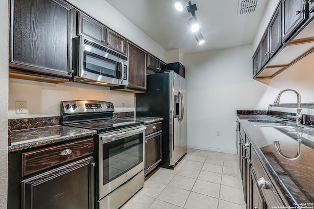 kitchen featuring dark brown cabinetry, rail lighting, sink, light tile patterned floors, and stainless steel appliances