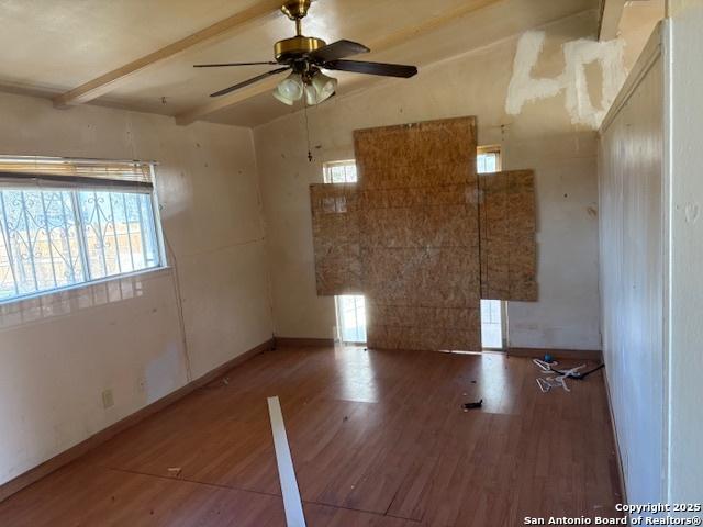 empty room with wood-type flooring, plenty of natural light, and beam ceiling