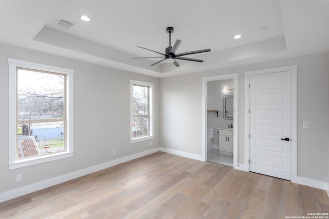 unfurnished bedroom featuring ensuite bathroom, a raised ceiling, and light hardwood / wood-style flooring