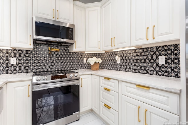 kitchen featuring stainless steel appliances, white cabinetry, light stone countertops, and decorative backsplash