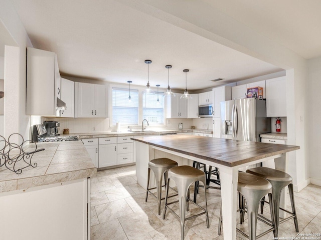 337 W Hackberry St, Fredericksburg, TX 78624 - kitchen with wall chimney exhaust hood, sink, a breakfast bar area, white cabinetry, and stainless steel appliances