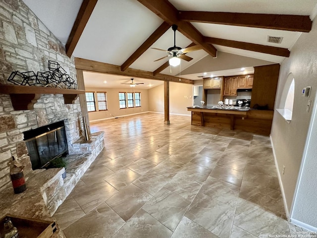 living room with vaulted ceiling with beams, a stone fireplace, and ceiling fan