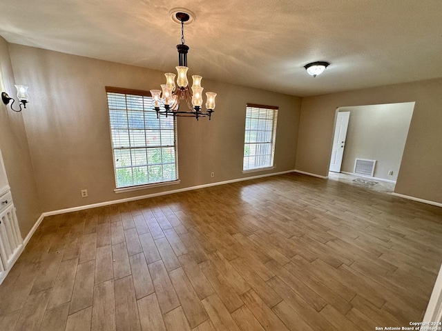 spare room featuring light hardwood / wood-style floors, a textured ceiling, and a notable chandelier