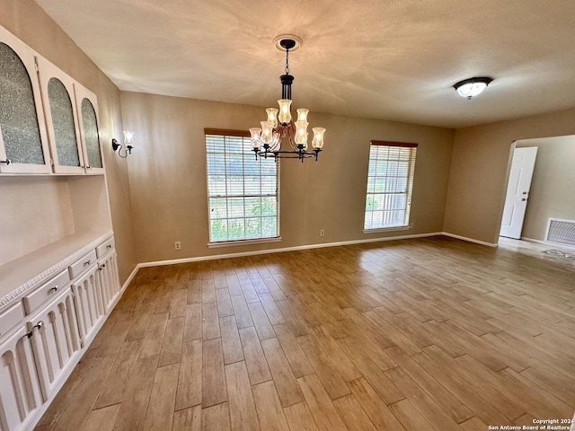 unfurnished dining area with a textured ceiling, a chandelier, and light hardwood / wood-style flooring