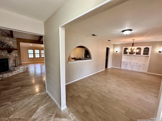 unfurnished living room featuring built in features, hardwood / wood-style floors, a notable chandelier, a fireplace, and a textured ceiling