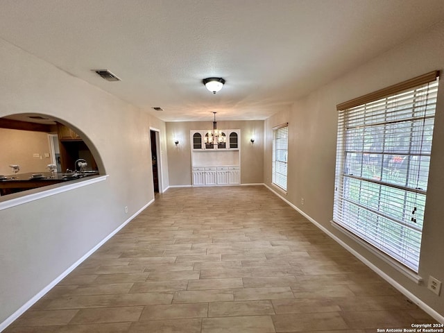 hall with a textured ceiling, an inviting chandelier, and light hardwood / wood-style flooring