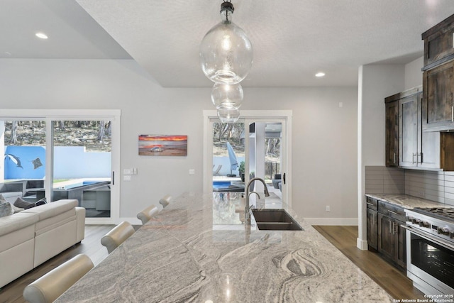 kitchen with decorative light fixtures, high end stove, sink, dark brown cabinetry, and light stone countertops