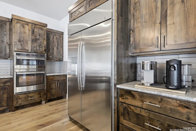 kitchen with light hardwood / wood-style flooring, stainless steel appliances, tasteful backsplash, light stone counters, and dark brown cabinetry