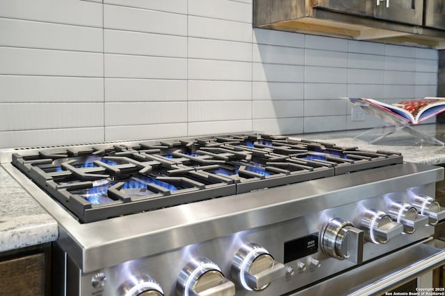 details with light stone counters, dark brown cabinetry, gas stove, and tasteful backsplash