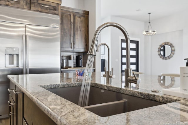 kitchen with built in refrigerator, light stone countertops, sink, and decorative light fixtures