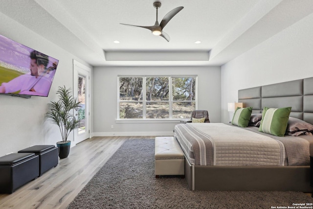 bedroom with ceiling fan, a raised ceiling, light hardwood / wood-style flooring, and access to outside