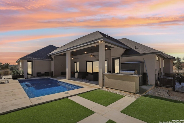 pool at dusk with ceiling fan, an outdoor living space, exterior kitchen, and a patio