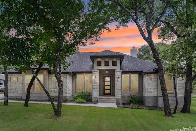 prairie-style house with a front yard, stone siding, roof with shingles, and a chimney