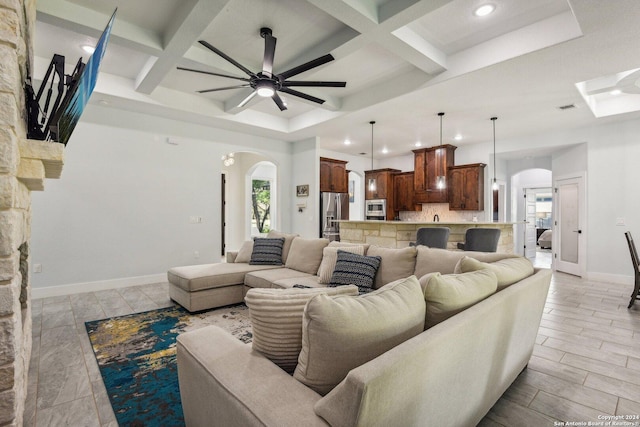 living area with baseboards, arched walkways, coffered ceiling, a ceiling fan, and beamed ceiling