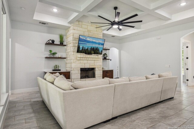 living room with coffered ceiling, arched walkways, visible vents, and a stone fireplace