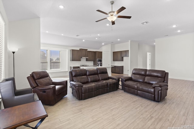 living room with ceiling fan, lofted ceiling, sink, and light hardwood / wood-style flooring