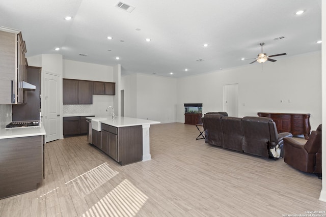 kitchen featuring sink, tasteful backsplash, light hardwood / wood-style floors, a center island with sink, and stainless steel gas stovetop