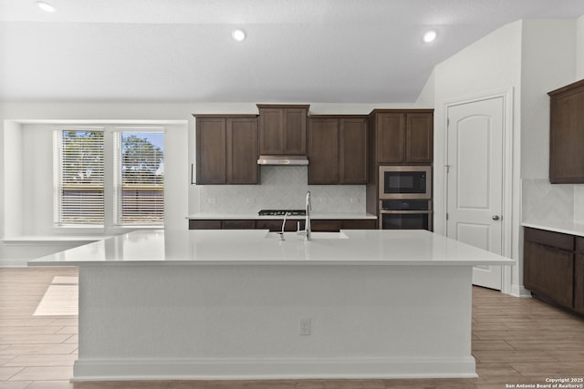 kitchen featuring dark brown cabinets, appliances with stainless steel finishes, a center island with sink, and backsplash