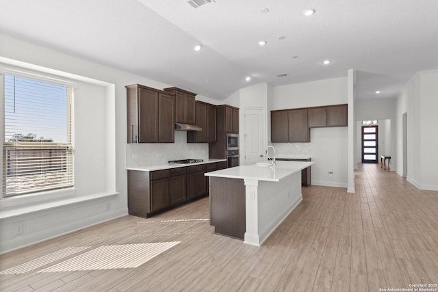 kitchen with appliances with stainless steel finishes, sink, decorative backsplash, a kitchen island with sink, and light hardwood / wood-style flooring