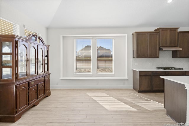 kitchen featuring lofted ceiling, gas stovetop, dark brown cabinets, and tasteful backsplash