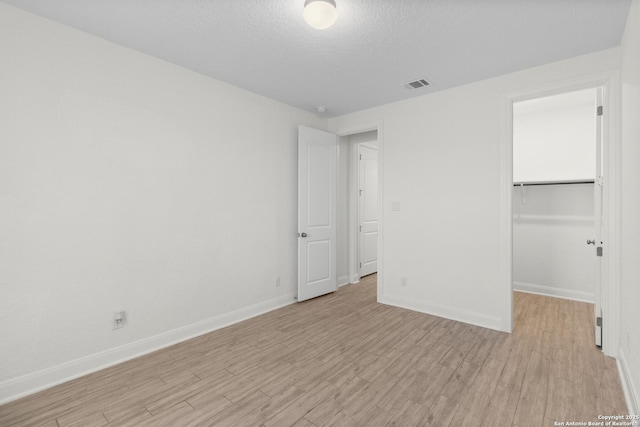 unfurnished bedroom featuring a closet, a spacious closet, a textured ceiling, and light wood-type flooring