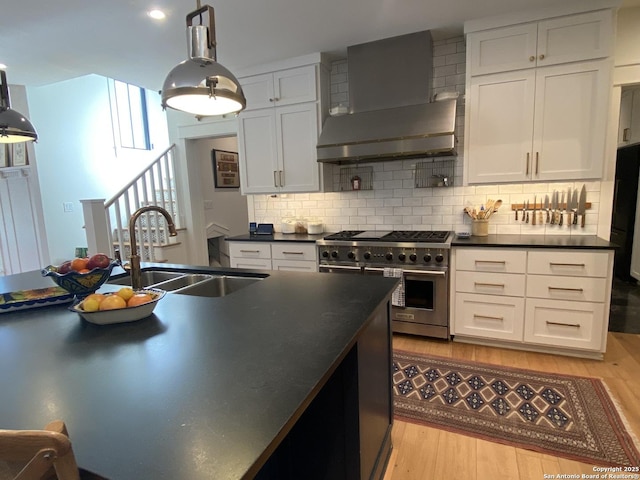 kitchen with wall chimney exhaust hood, dark countertops, a sink, and high end range