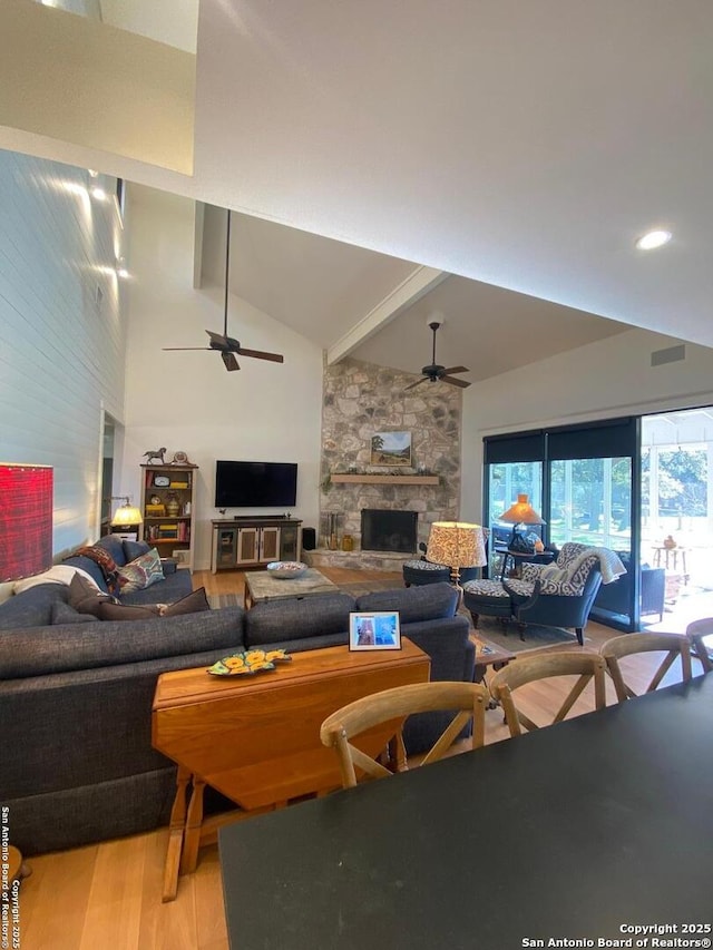 living area featuring high vaulted ceiling, a fireplace, wood finished floors, a ceiling fan, and beamed ceiling