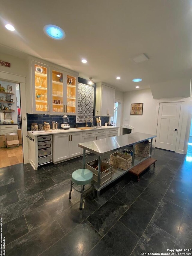 kitchen with a sink, white cabinetry, light countertops, tasteful backsplash, and glass insert cabinets