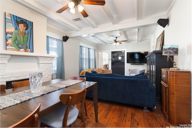 living room with dark wood-type flooring, ceiling fan, a stone fireplace, and beamed ceiling