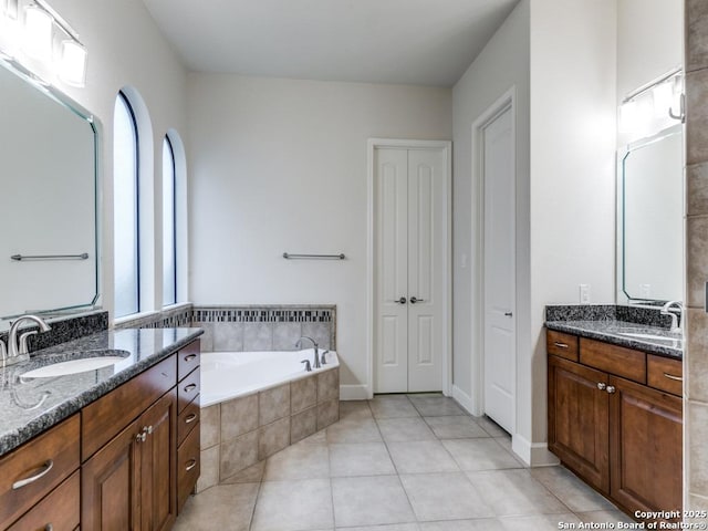 bathroom with a relaxing tiled tub, vanity, and tile patterned flooring