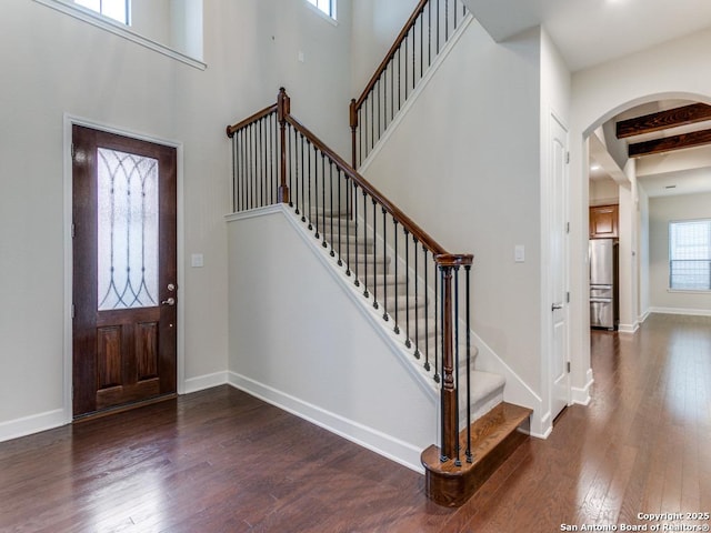 foyer featuring beam ceiling, dark wood-type flooring, and a towering ceiling