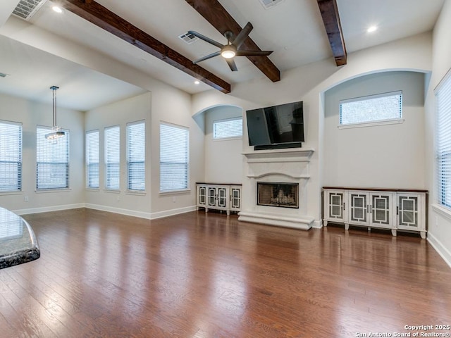 unfurnished living room featuring beamed ceiling, ceiling fan, a healthy amount of sunlight, and dark hardwood / wood-style flooring