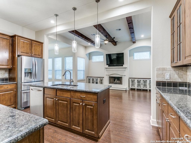 kitchen with dark hardwood / wood-style floors, sink, dark stone countertops, stainless steel appliances, and a center island with sink