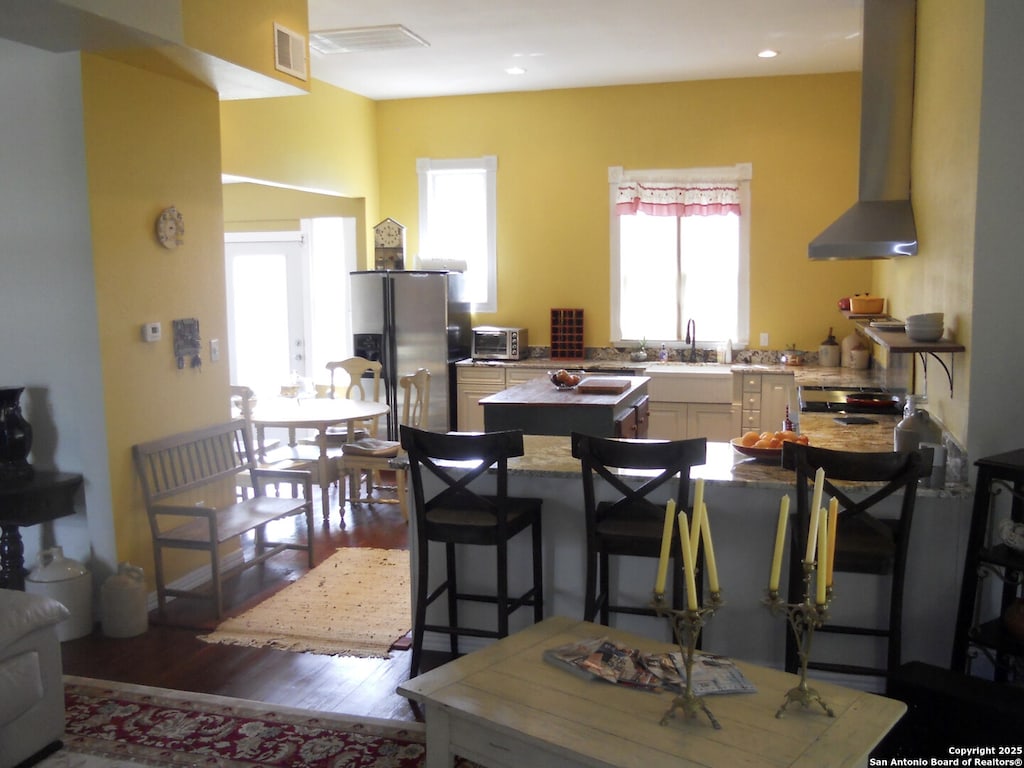 kitchen with stainless steel fridge, a kitchen breakfast bar, range, wall chimney range hood, and light wood-type flooring