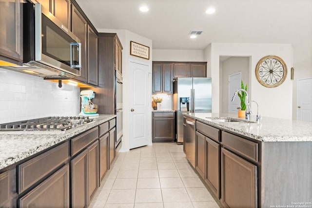 kitchen with light stone counters, stainless steel appliances, sink, and a center island with sink